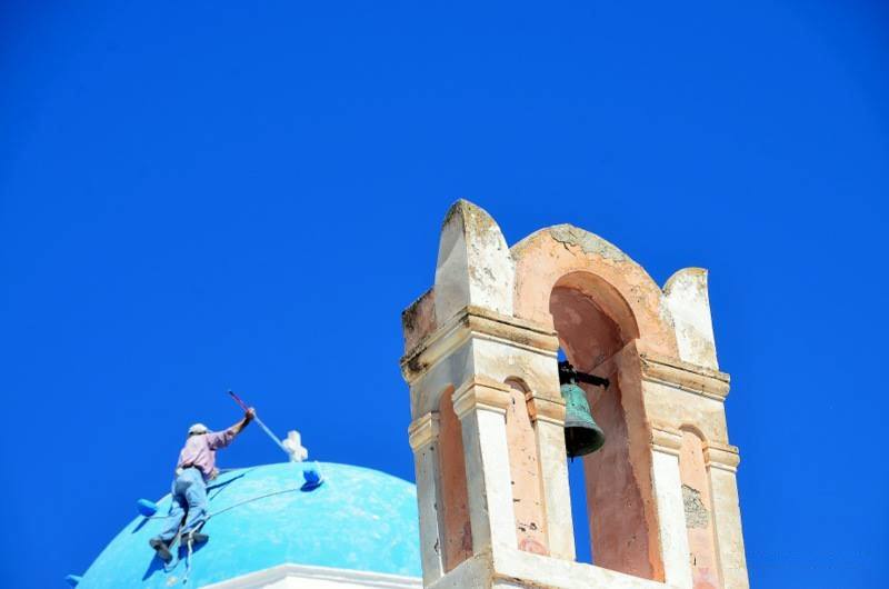 a man hand-painting a famous blue dome; much like creating that beautiful color, being a reliable travel advisor partner in santorini takes passion and hard work