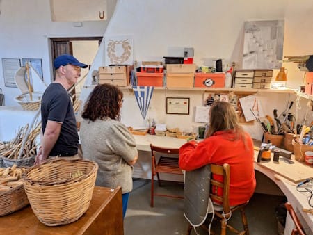 Yannis Pantazis at Symposion, sitting at his work bench and talking to my clients; one of the best hidden gems to include in a Santorini private tour away from crowds