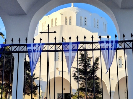 Santorini on May 5. What the Saint Irene Holiday Means for the Island and Your Stay, the image of Methropolitan Cathedral in Fira with festive greek flags on the railing